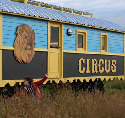 un enfant jouant devant une roulotte bleue et noire qui porte l'inscription stylisée "CIRCUS"